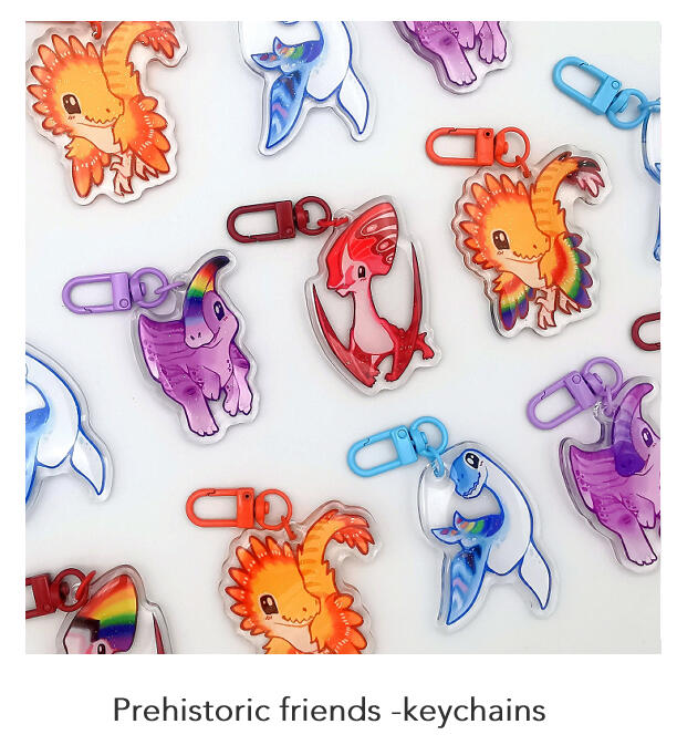 A photograph of numerous acrylic keychain charms featuring cute chibi dinosaurs.